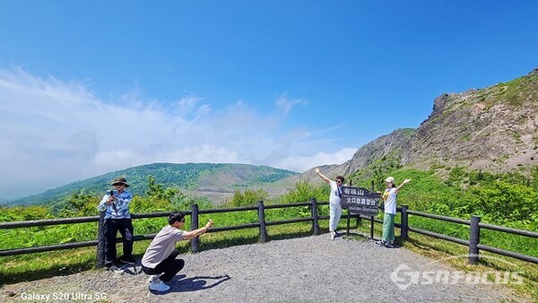 케이블카로 올라온 관광객이 우스산 분화구 안내판 배경으로 인증샷 찍고 있다.  사진/유우상 기자